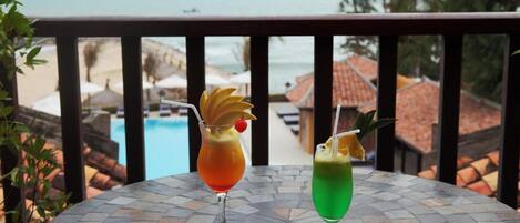 Two cocktails on a mosaic table with a view of a pool and beach in the background.