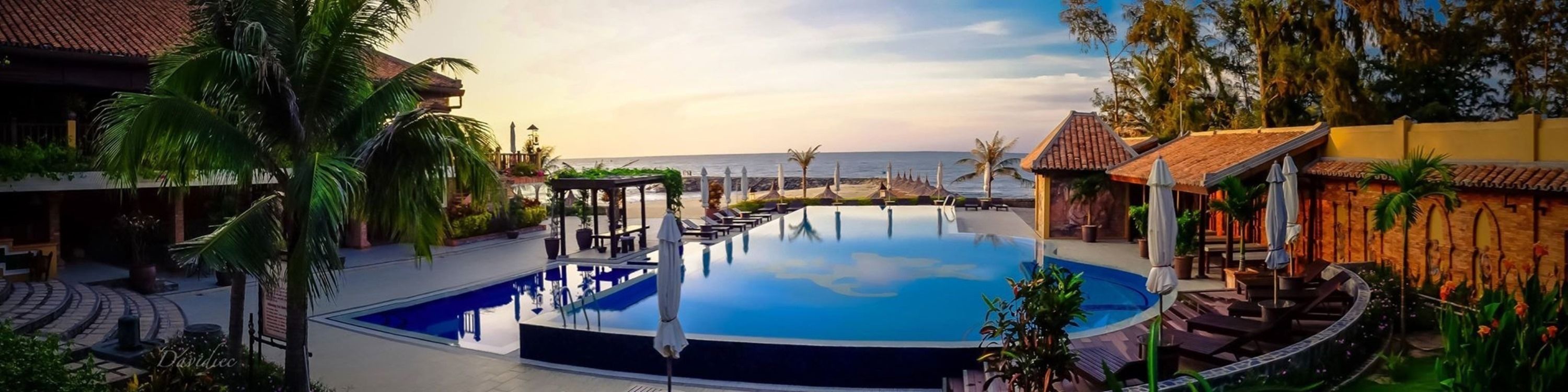 A pool area with a view of the ocean, surrounded by palm trees and lounge chairs.