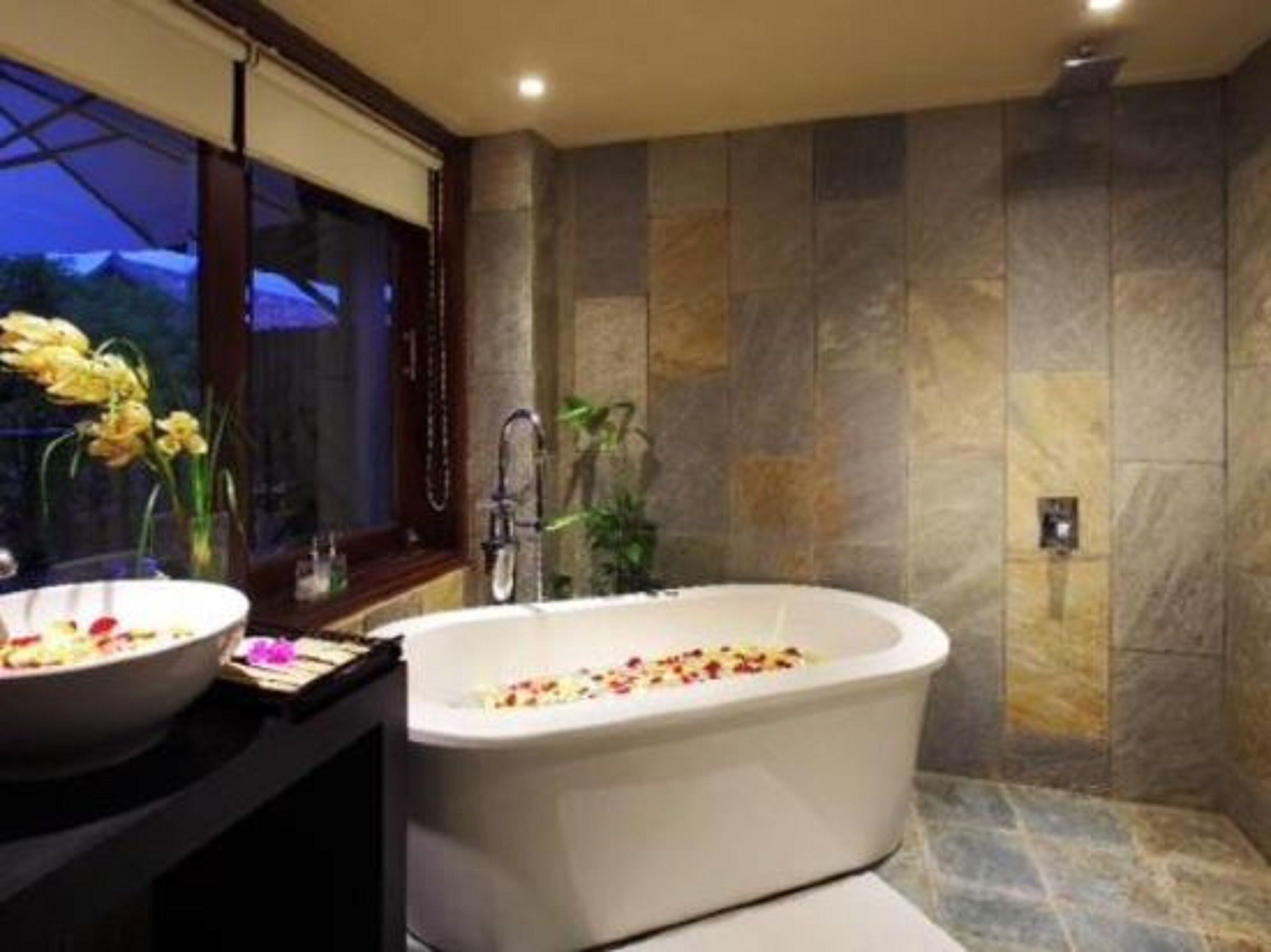 Une salle de bain moderne avec une baignoire sur pieds, une grande fenêtre et un mur en pierre.