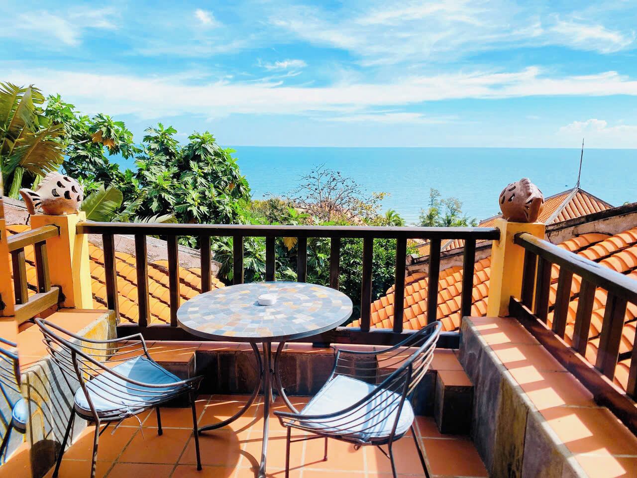 A terrace with a round table and chairs, a view of the sea, and a railing.