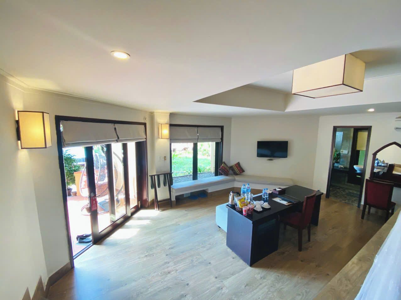 A spacious living area with a large sliding glass door, a dining table with chairs, a bench, and a flat-screen TV mounted on the wall.