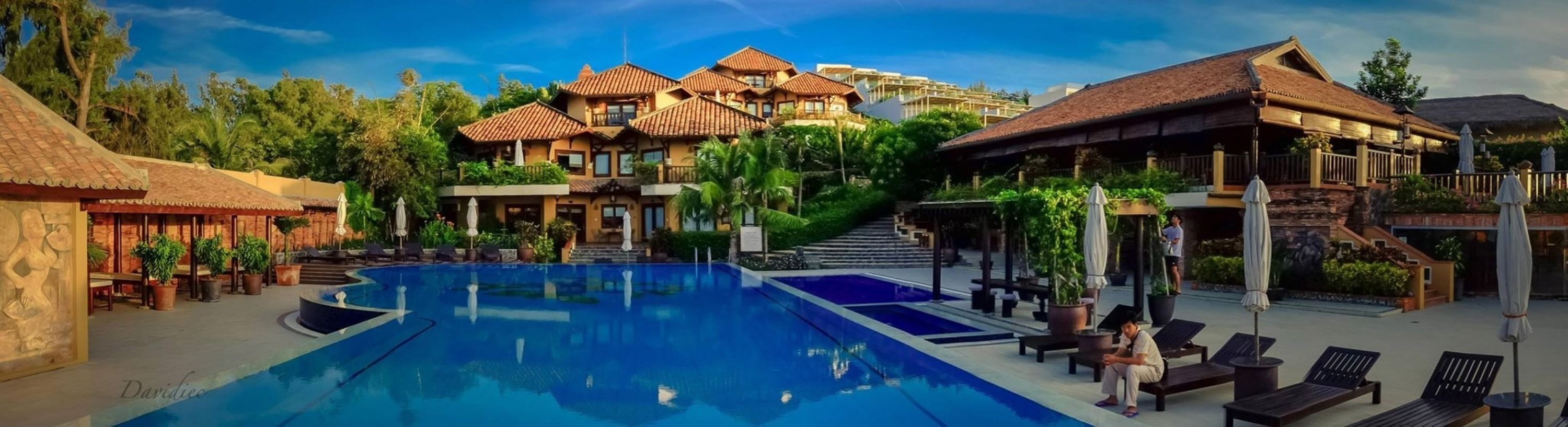Un resort con una piscina grande, mobiliario exterior y un edificio con techo de tejas.