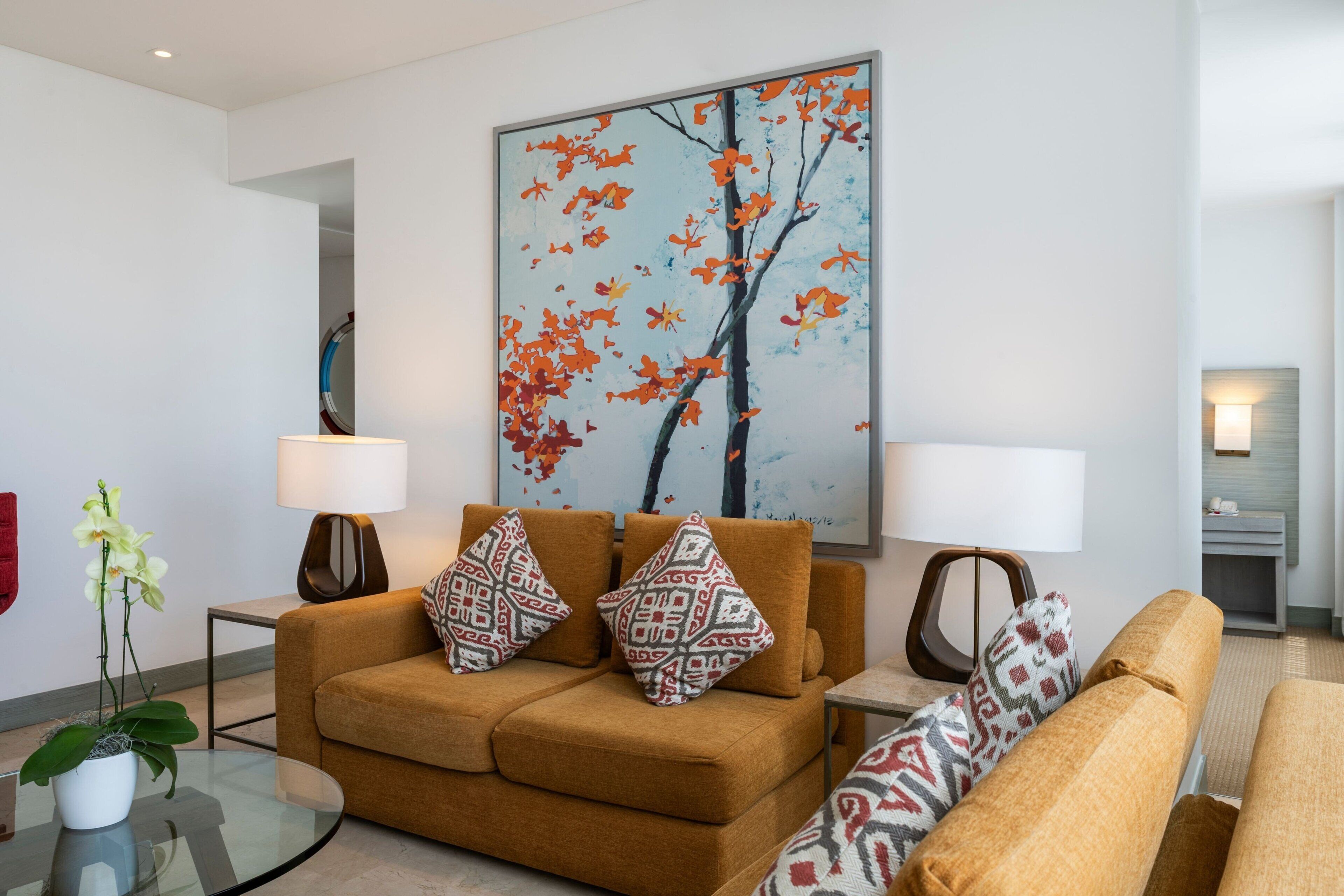 Een moderne woonkamer met een bank, twee bijzettafeltjes, een vloerlamp en een groot abstract schilderij.