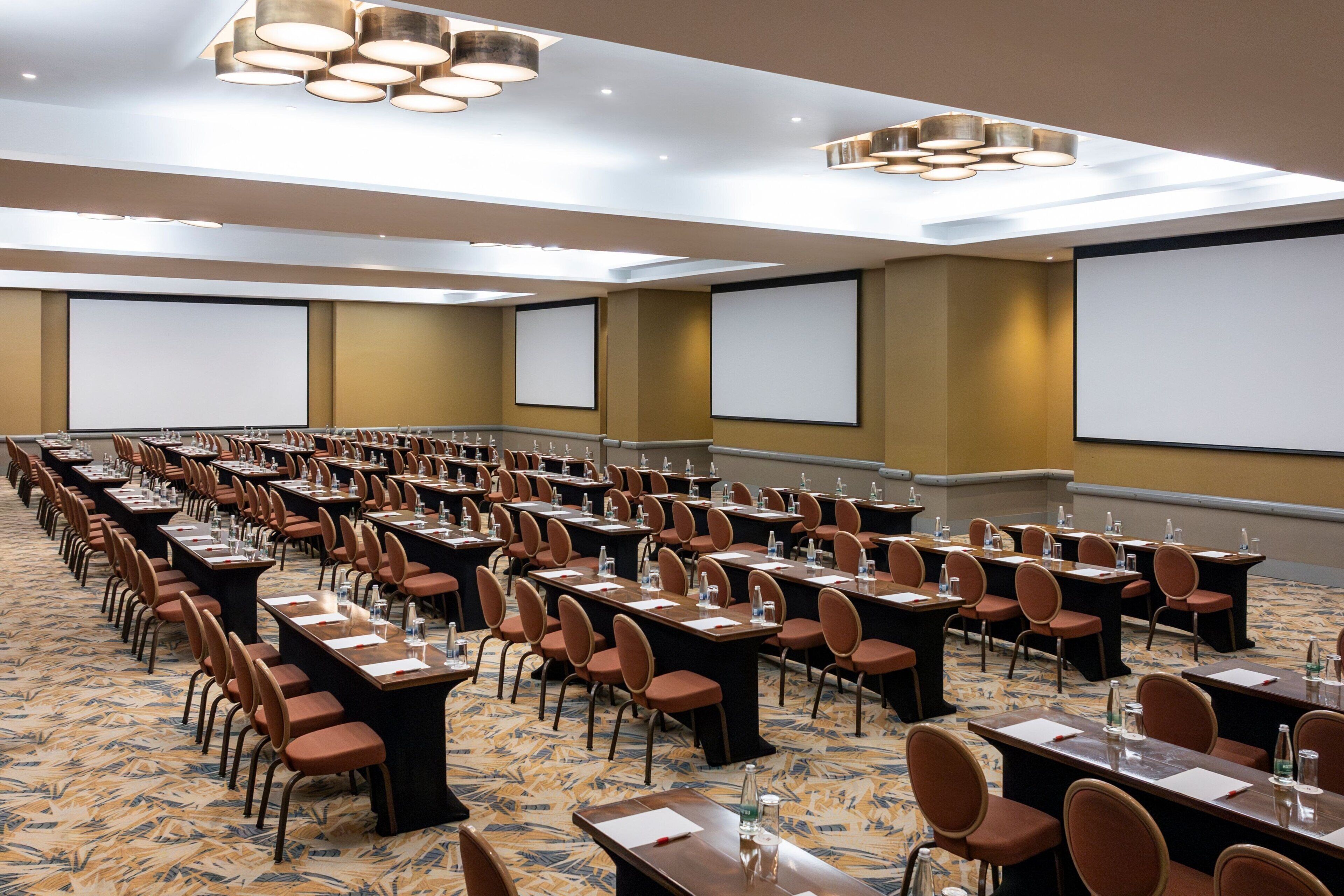 A conference room with rows of tables and chairs, equipped with projectors and screens.