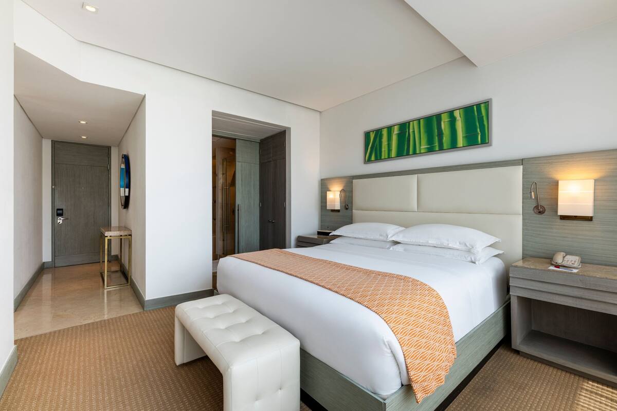 Ein modernes Hotelzimmer mit einem großen Bett, einem Nachttisch, einer Sitzbank und einem Wandbild.