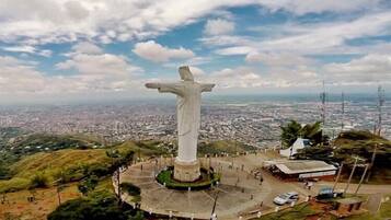 Una estatua grande de una figura con los brazos extendidos, rodeada por una plaza circular con algunos edificios y una carretera cercana.