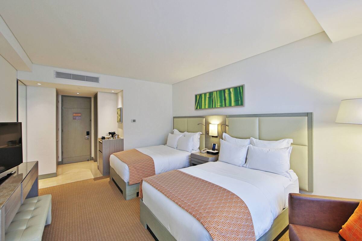 Ein Hotelzimmer mit zwei Betten, einem Fernseher, einem Schreibtisch und einem Sessel.