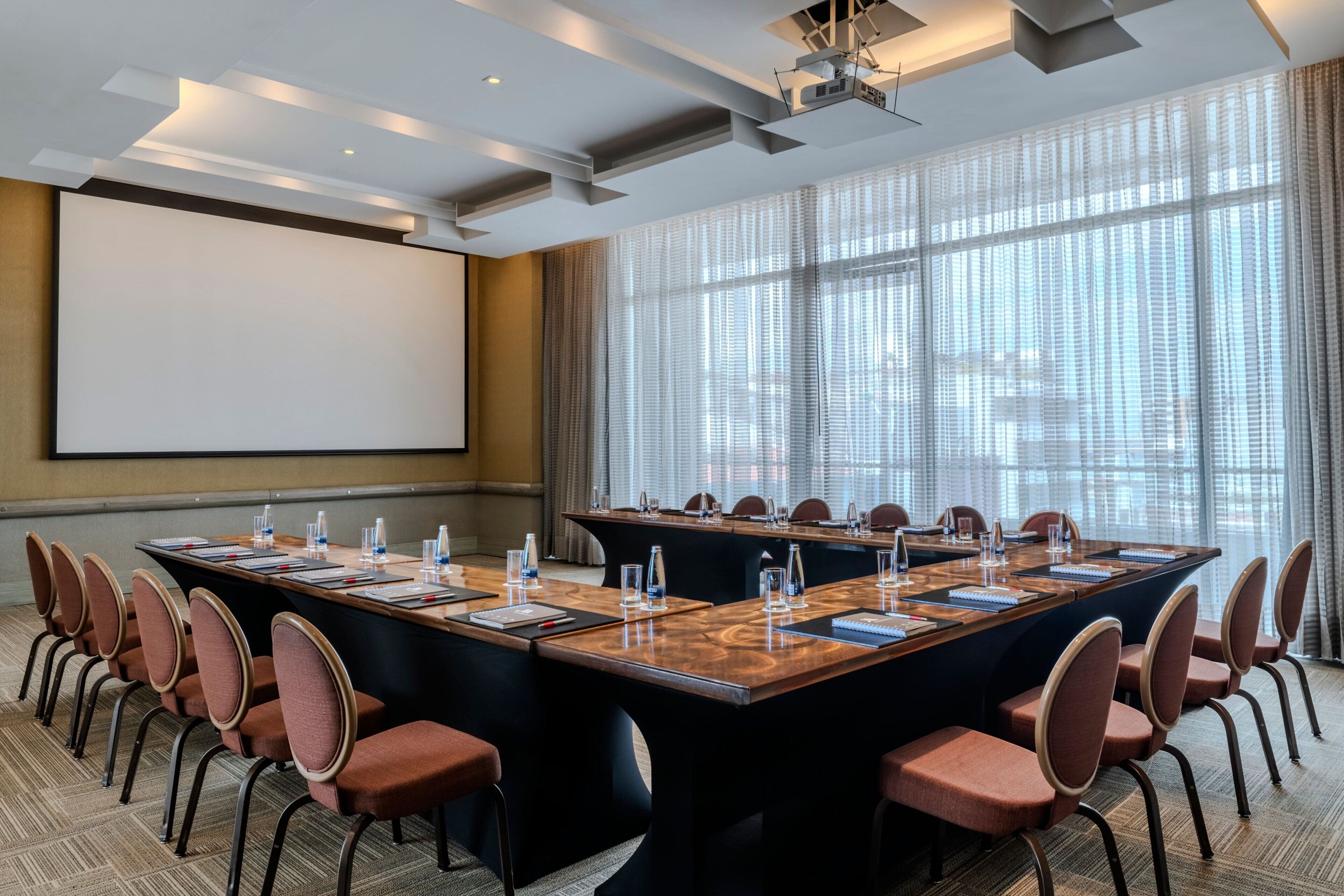 A conference room with a large table, chairs, a projector screen, and large windows.