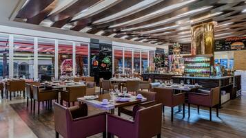 A modern restaurant with wooden ceiling panels, glass partitions, and a bar area with colorful decorations.