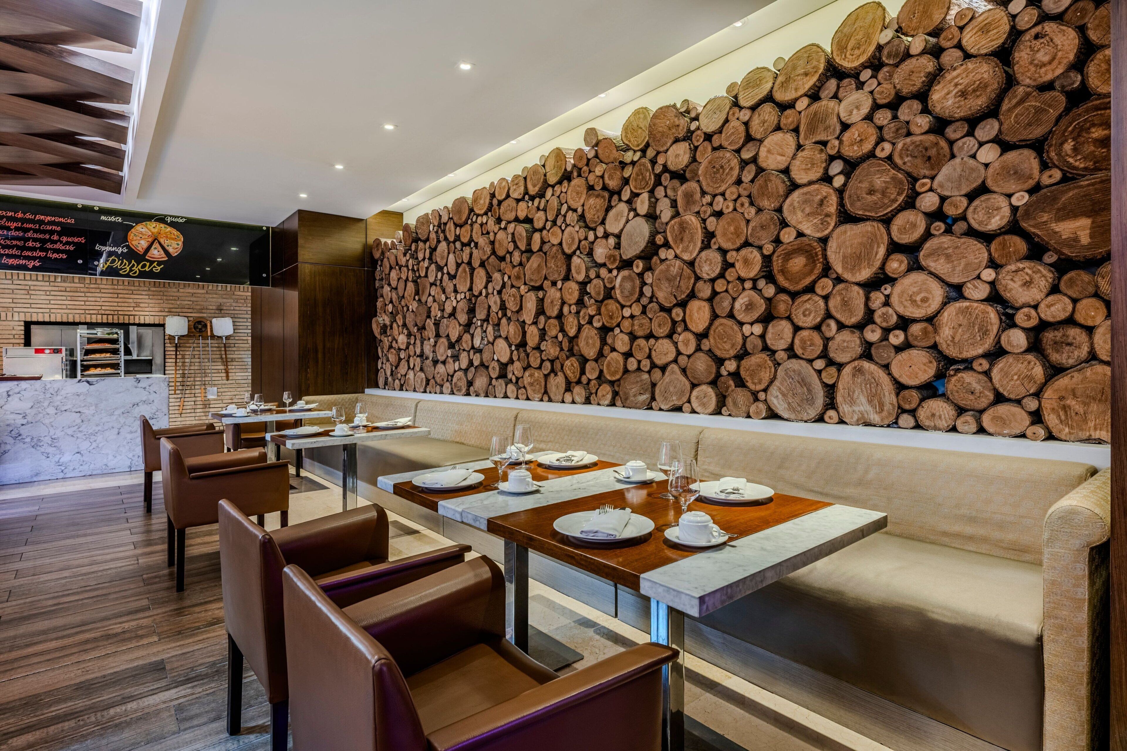 A restaurant with wooden log wall decor, marble tables, and leather chairs.