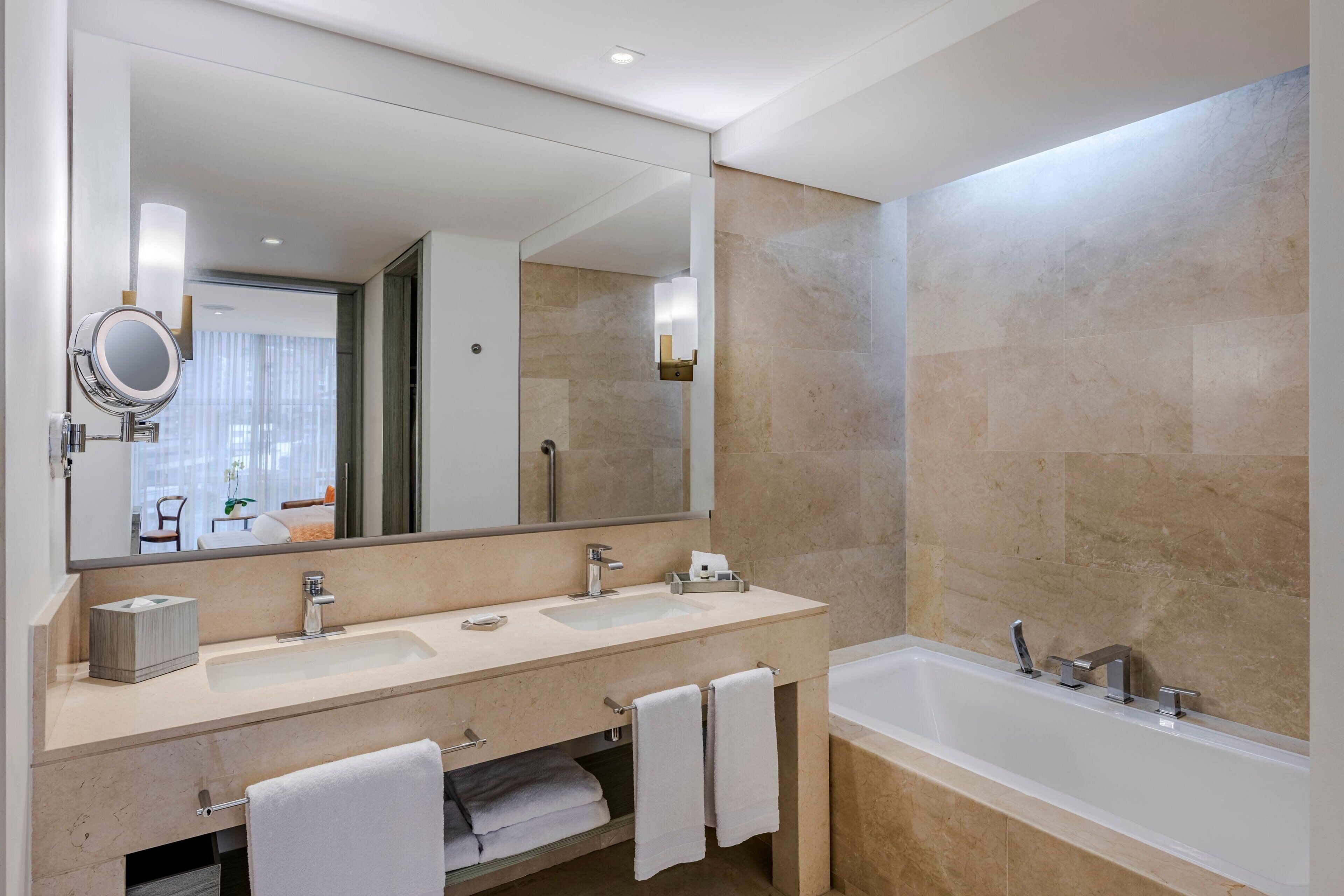 A modern bathroom with a large mirror, two sinks, a bathtub, and a towel rack.