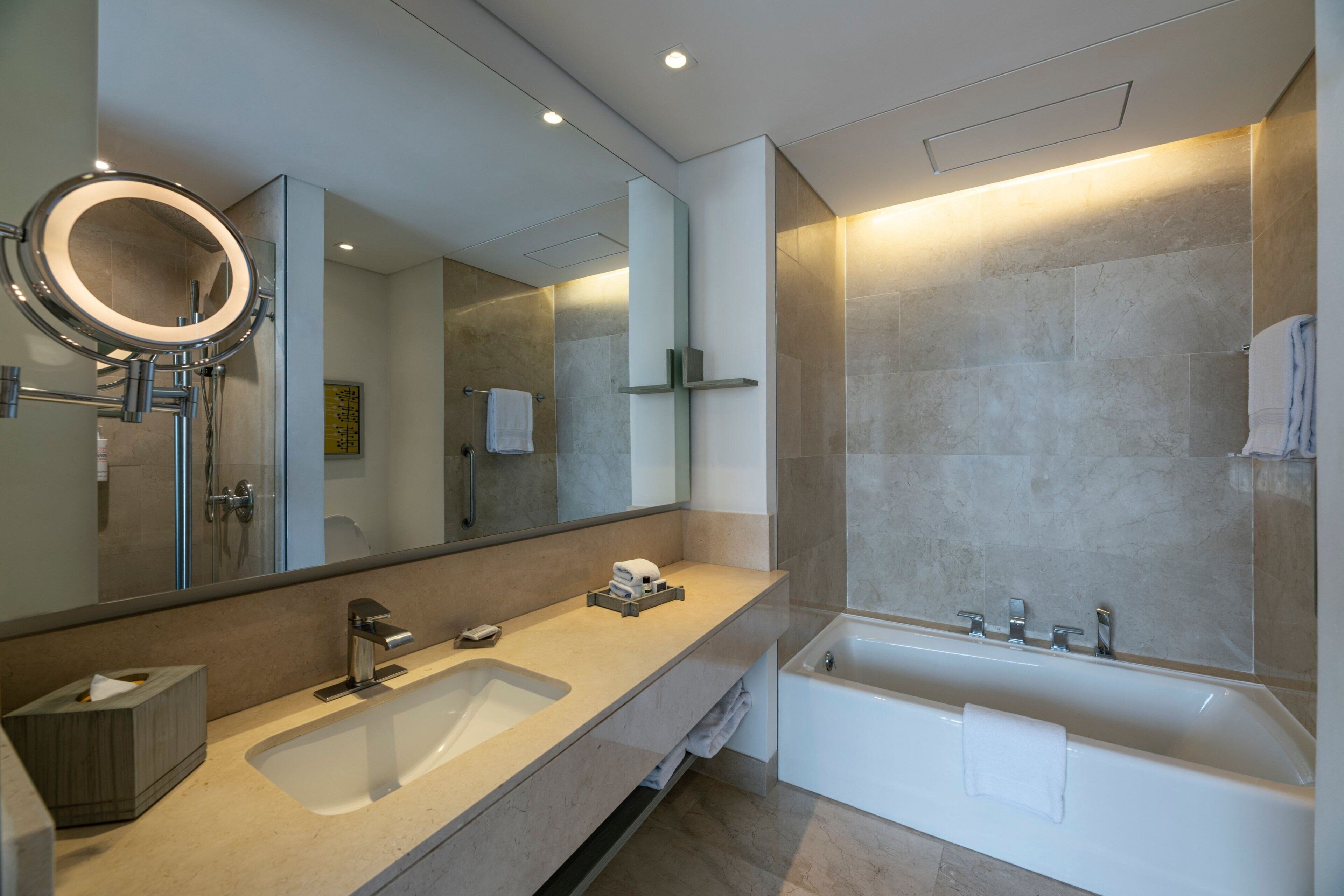 Un bany modern amb un lavabo gran, una banyera i un mirall amb marc circular.