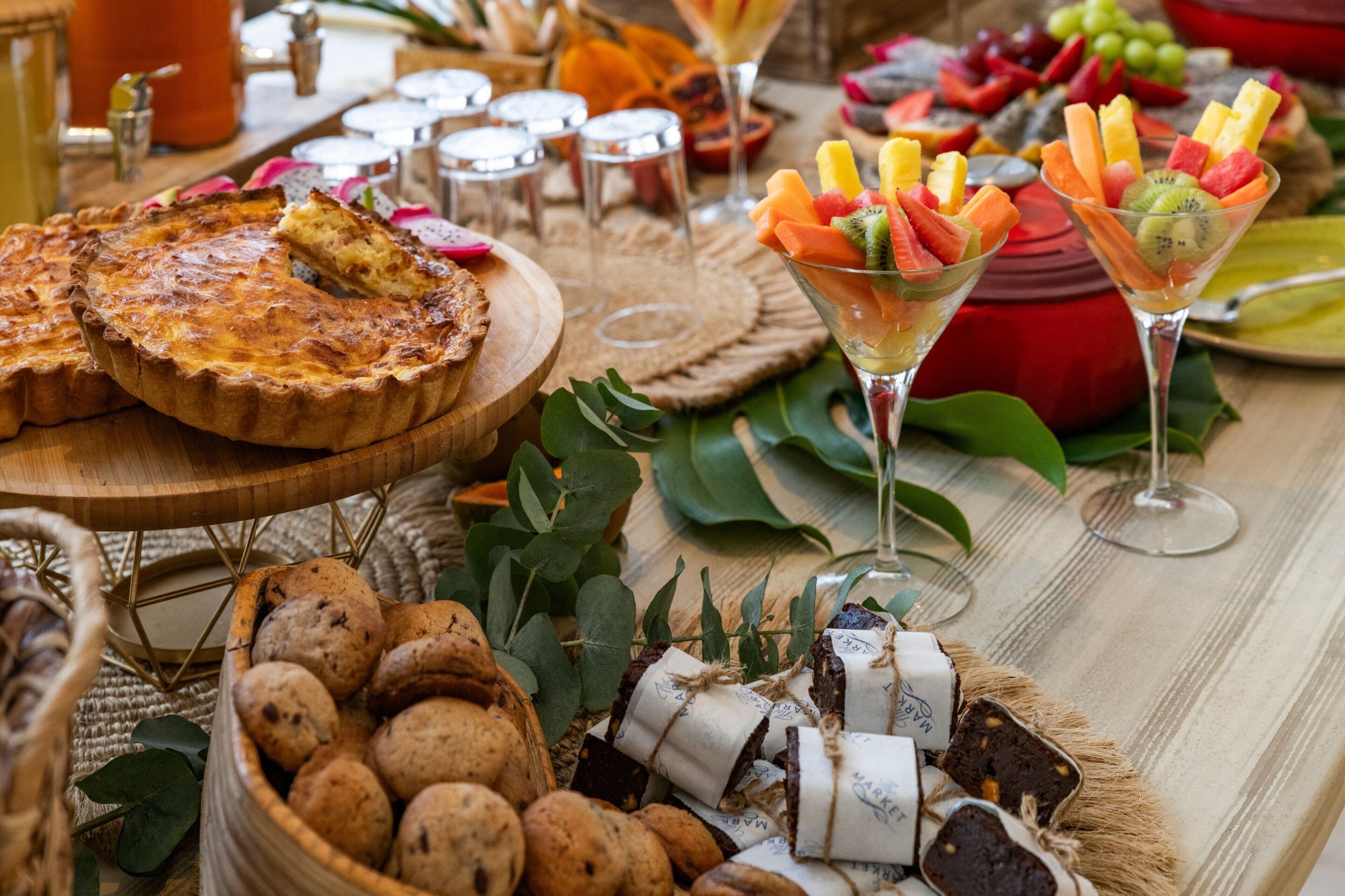 Ein Tisch mit verschiedenen Speisen, darunter Quiche, Obstspieße und eine Auswahl an Brot.