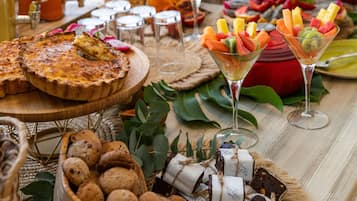 Una mesa con diversos alimentos, incluyendo una quiche, brochetas de fruta y panes variados.