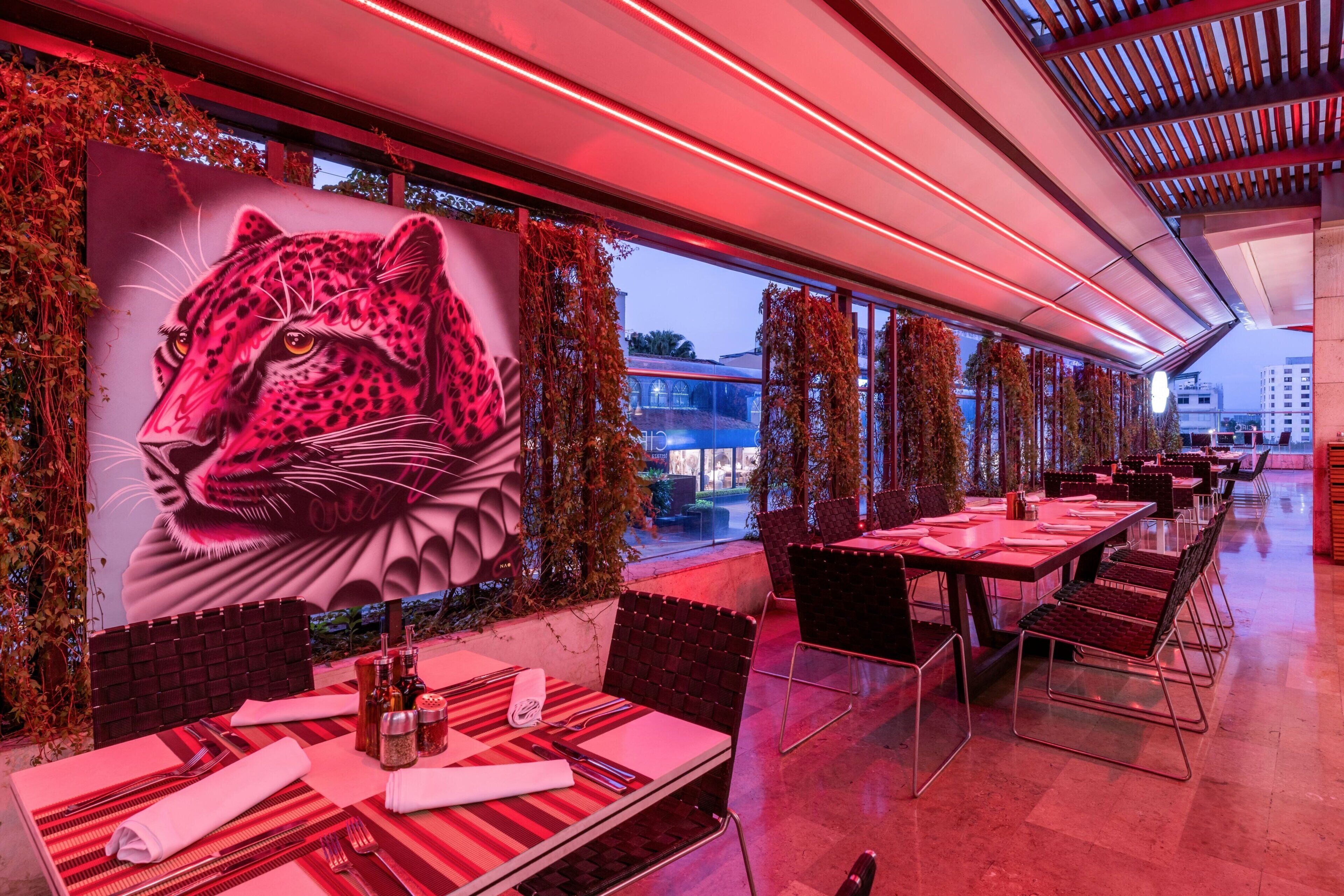 Un restaurant orné d’une grande fresque représentant un léopard, doté d’une terrasse et d’un éclairage d’ambiance rouge.
