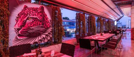 Un restaurante con un gran mural de leopardo, mesas al aire libre e iluminación ambiental roja.
