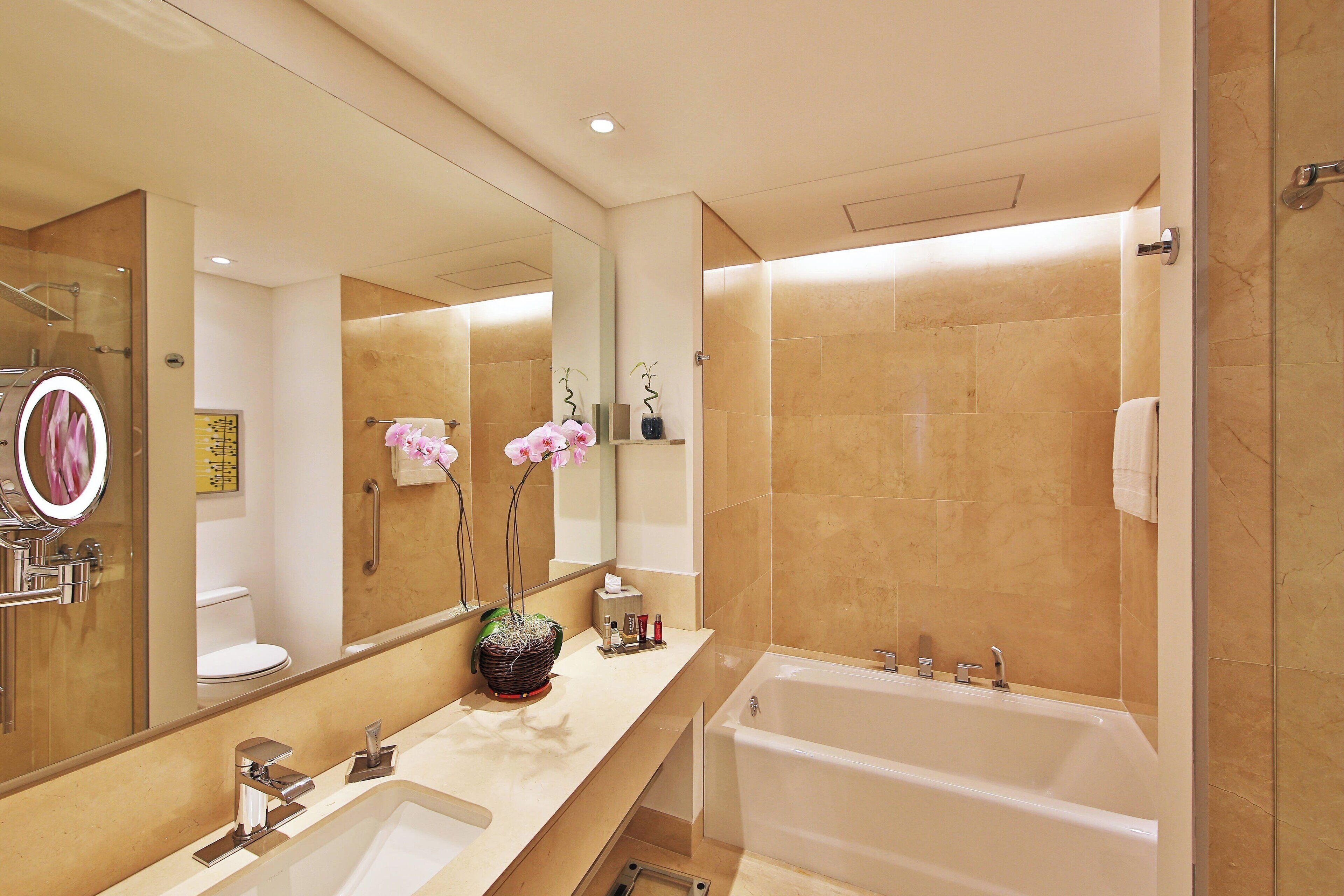 Une salle de bain moderne avec un grand miroir, une baignoire et un lavabo.