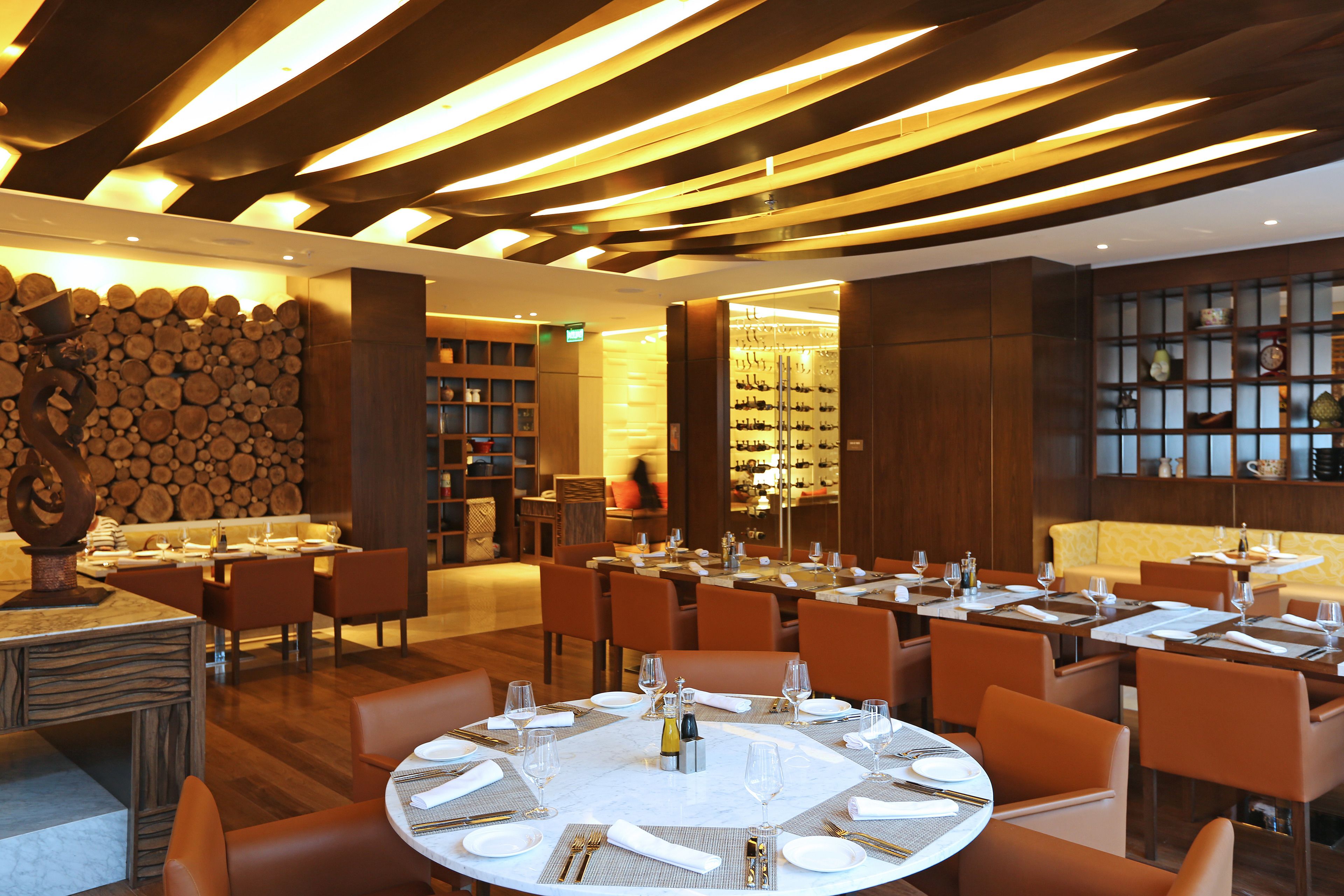 A restaurant with round tables, orange chairs, and a wooden ceiling.