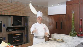 Een kok in een keuken met bakstenen muren, een marmeren werkblad en een pizzaoven.