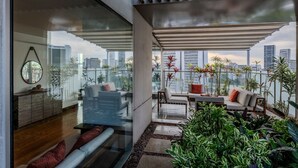 Ein modernes Wohnzimmer mit Glaswand, einer Couch, einem Couchtisch und Blick auf die Stadtlandschaft.