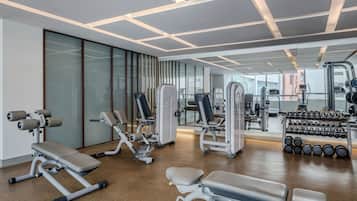 A modern gym with various exercise equipment, large windows, and a polished floor.