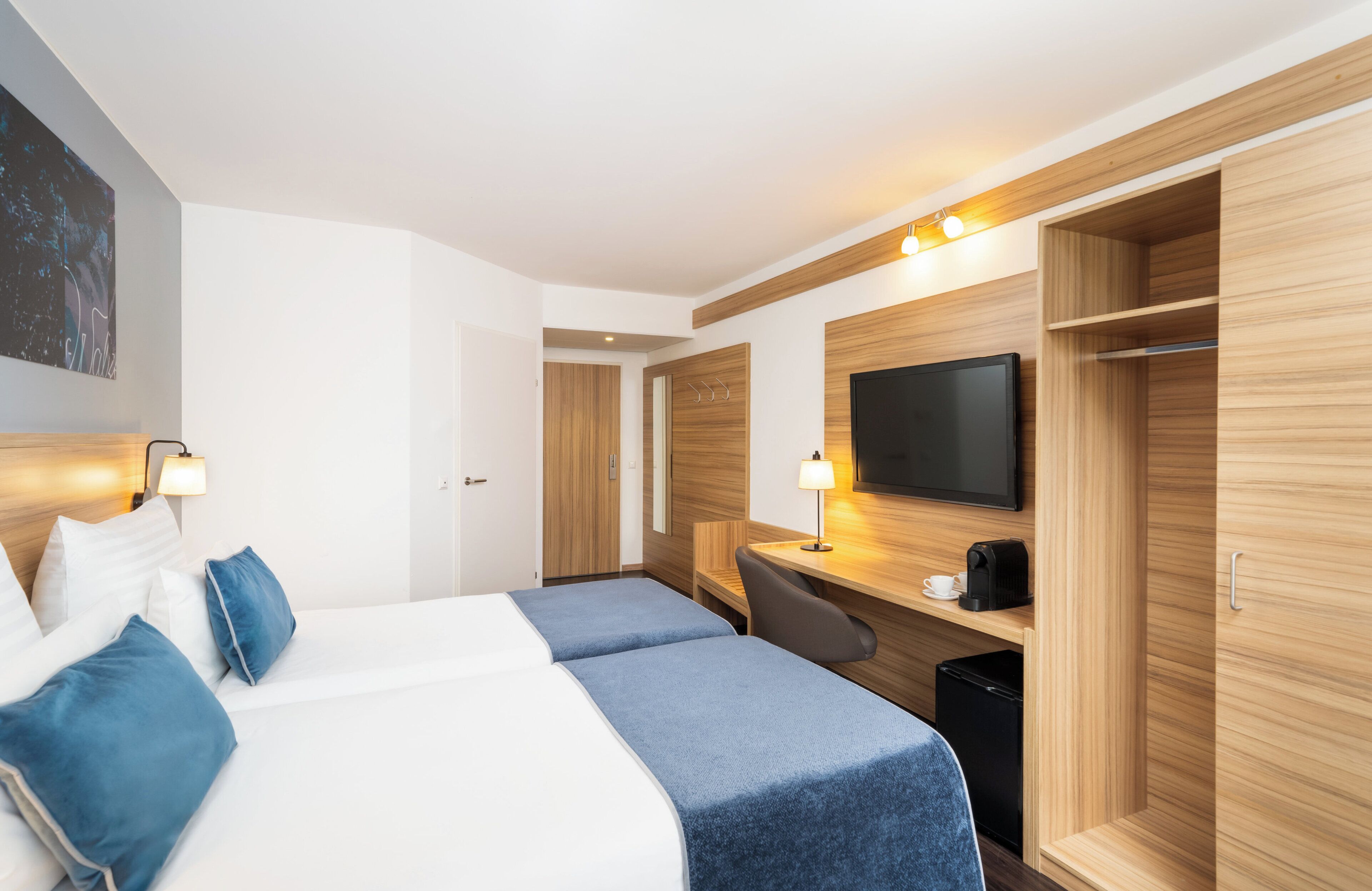 A hotel room with two beds, a desk, a television, and a wardrobe.