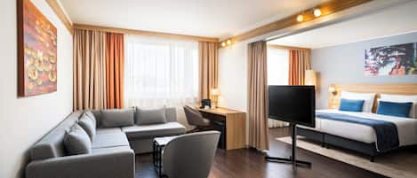A modern hotel room with a sofa, desk, TV, and a bed.