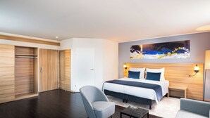 Een moderne hotelkamer met een groot bed, een stoel, een klein tafeltje en een schilderij aan de muur.
