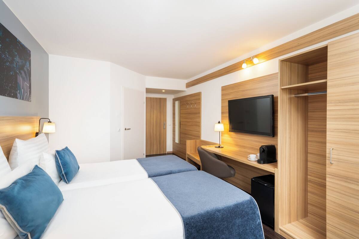 A hotel room with two beds, a desk, a television, and a wardrobe.