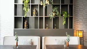 Een moderne eetruimte met een donkerhouten tafel, twee comfortabele zitbanken en een decoratieve wand met planken en hangplanten.