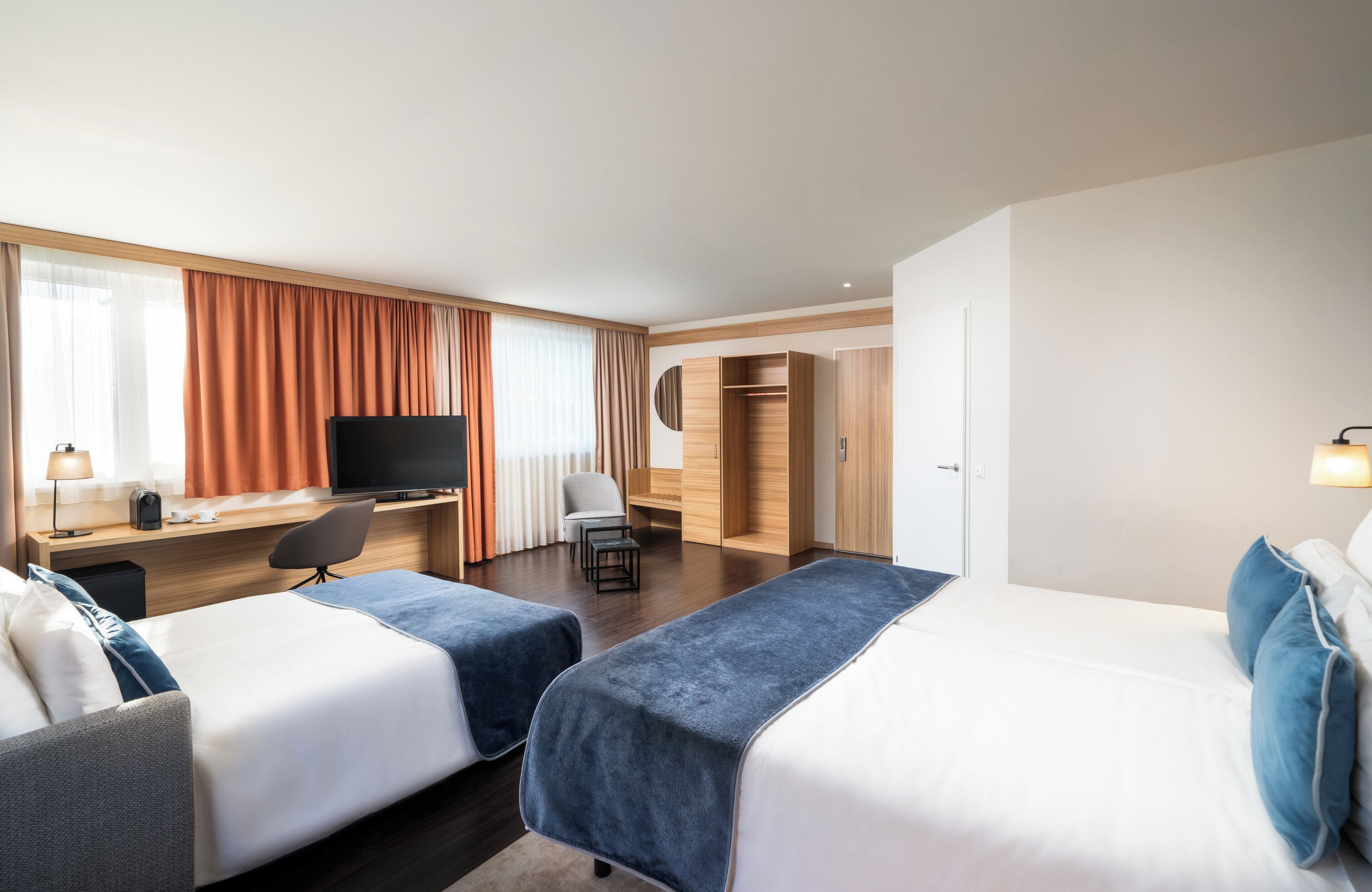 A hotel room with two beds, a desk with a TV, a chair, and a wardrobe.