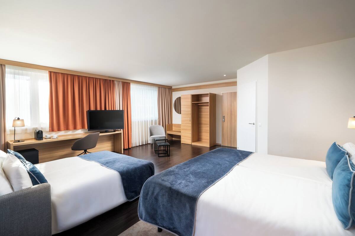 A hotel room with two beds, a desk with a TV, a chair, and a wardrobe.