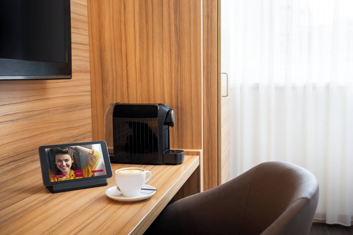 A wooden desk with a coffee maker, a tablet displaying a video call, and a cup of coffee.