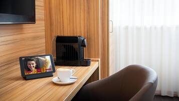 Habitació d'hotel amb un mur de panells de fusta, un televisor de pantalla plana muntat sobre una taula de fusta, una cafetera, una tassa de cafè i una tauleta mostrant una fotografia.