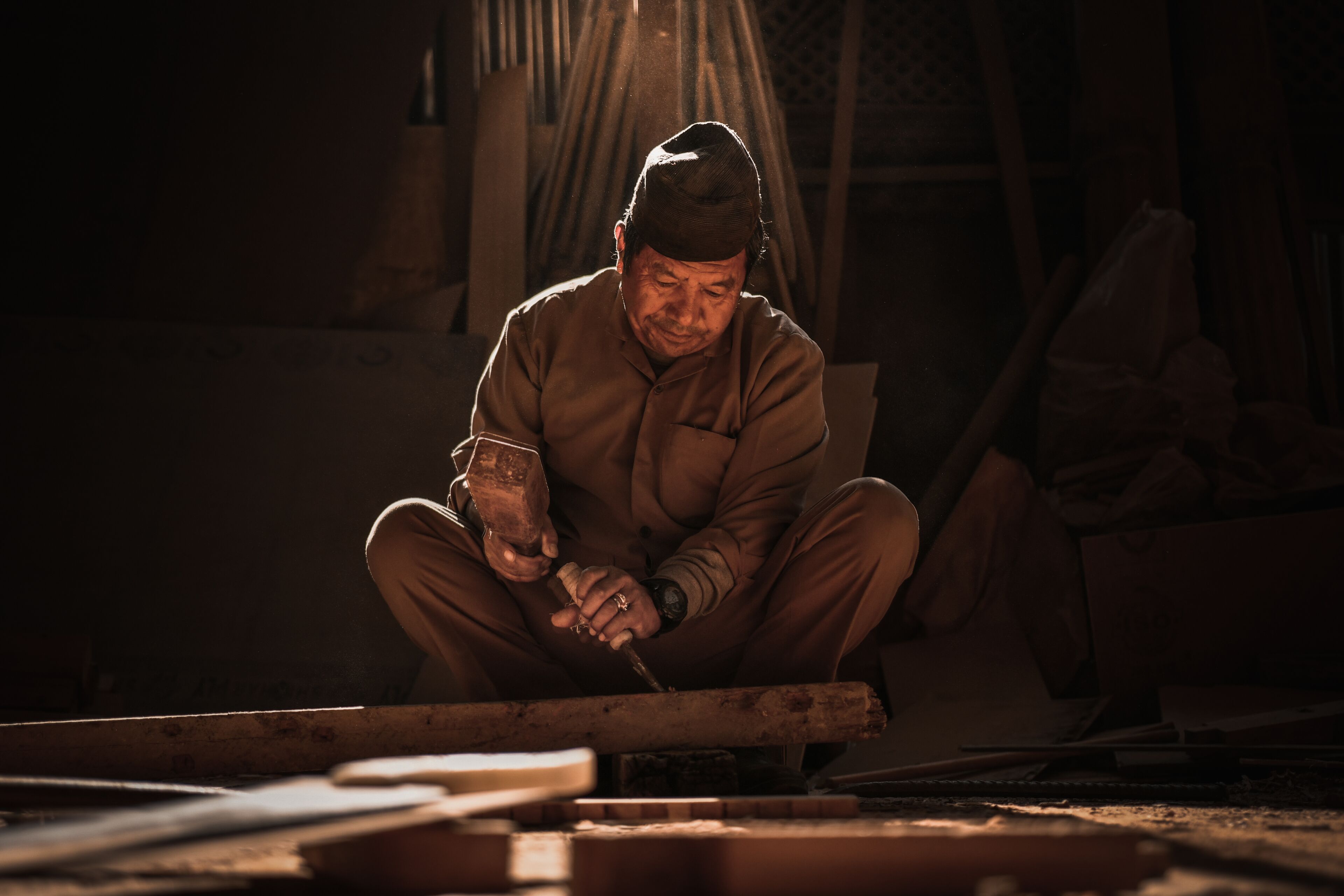 A person working with a tool on a wooden surface in a dimly lit room.