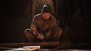 A person working with a tool on a wooden surface in a dimly lit room.