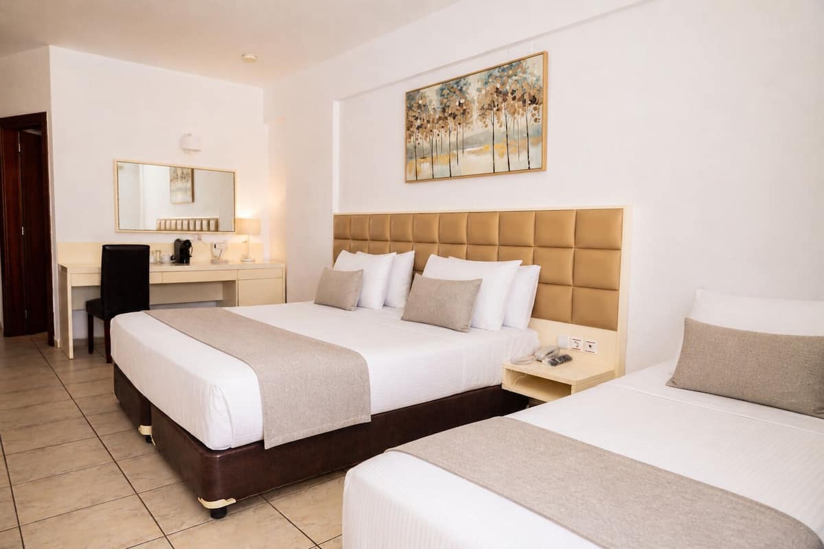 A hotel room with a large bed, a desk with a chair, a bedside table with a phone, and a painting on the wall.