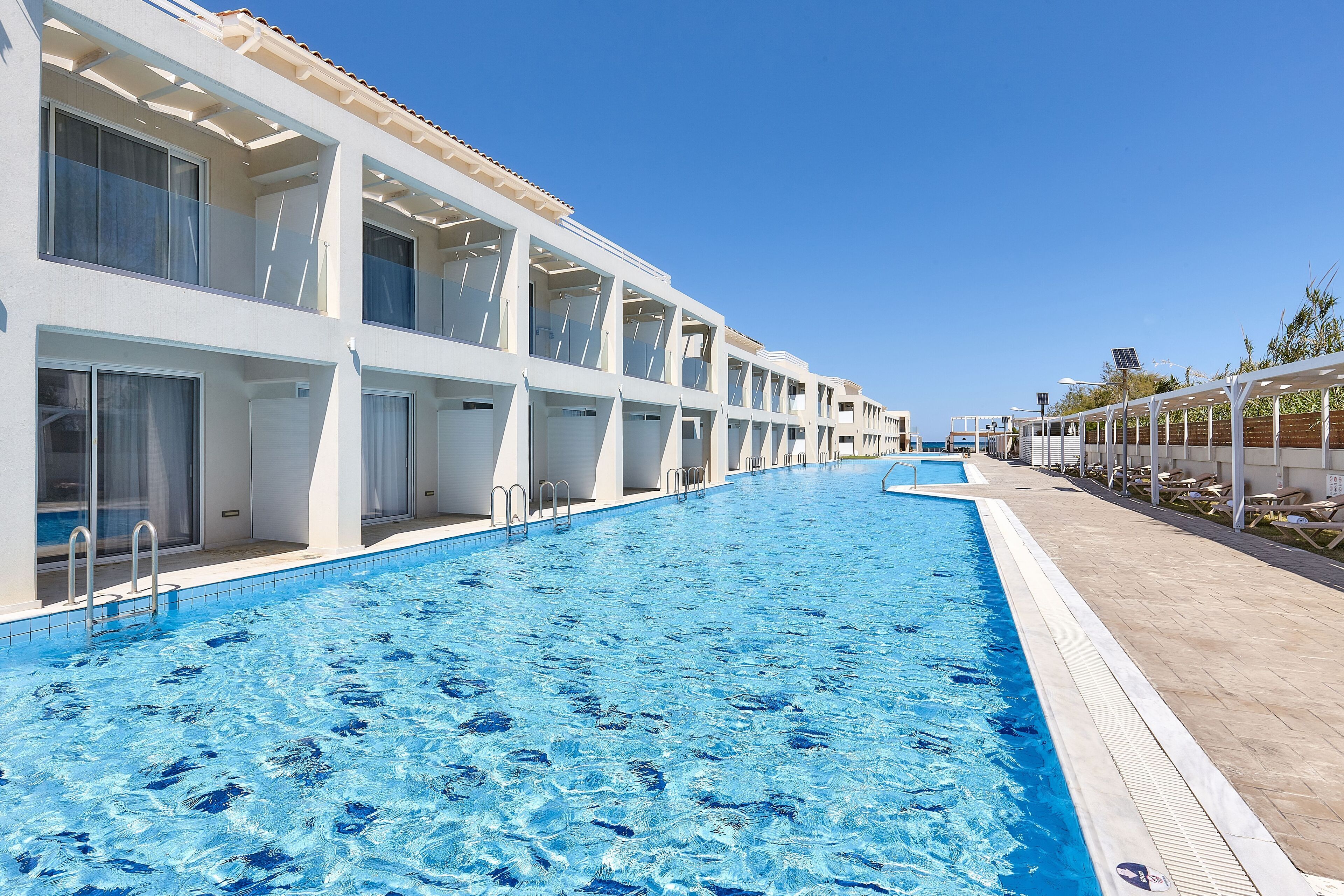 A swimming pool adjacent to a hotel with multiple balconies and a clear blue sky.