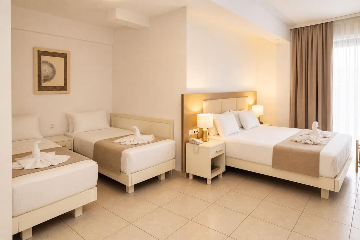A hotel room with two beds, a bedside table with a lamp, a framed picture on the wall, and a window with curtains.
