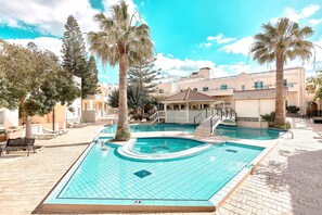 A swimming pool with a tiled deck, palm trees, and a building with a tiled roof in the background. - St. Constantin Beach Hotel and Spa (Hersonissos)