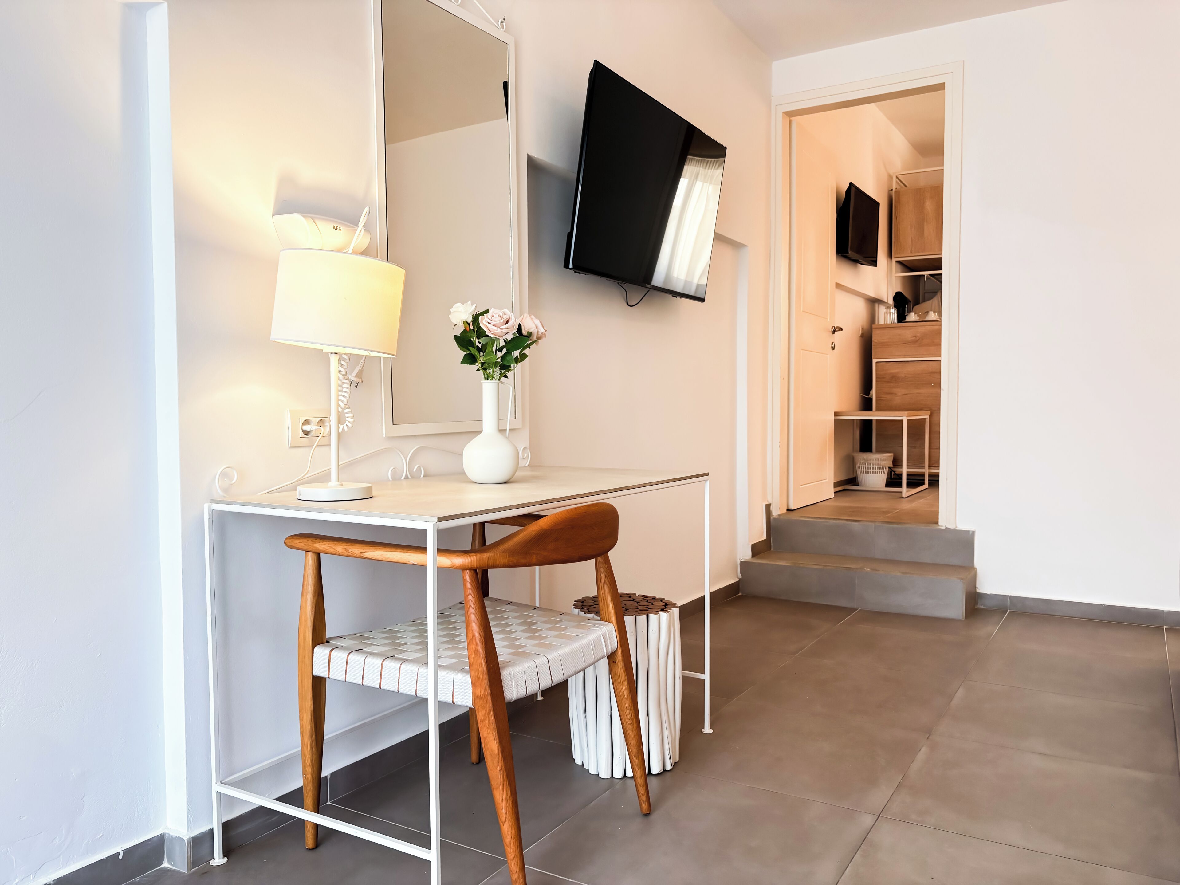 A modern room with a desk, chair, lamp, vase with flowers, and a TV mounted on the wall.