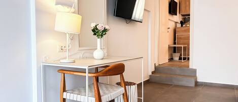A modern room with a desk, chair, lamp, vase with flowers, and a TV mounted on the wall.
