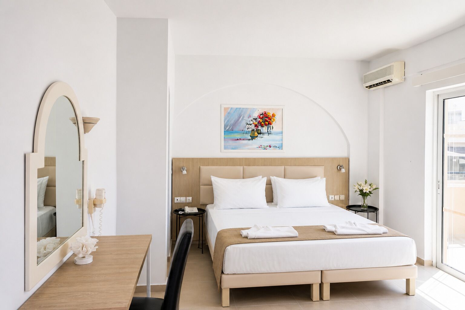 Una habitación de hotel con cama, mesitas de noche, escritorio, silla, espejo y ventana.