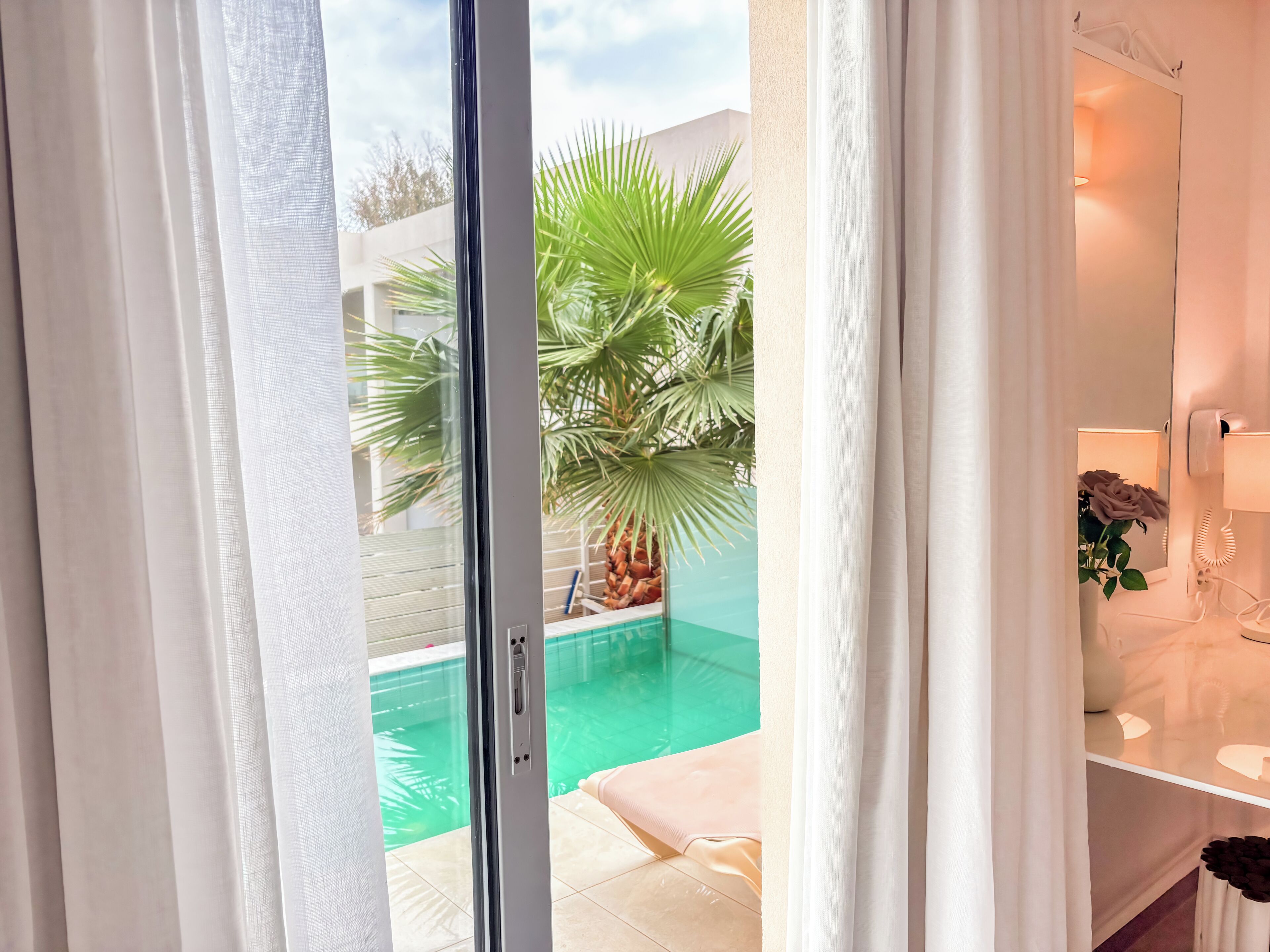 A room with a sliding glass door leading to a swimming pool, a potted plant, and a white shelf with a vase.
