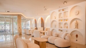 A modern lounge area with plush seating, a central coffee table, and a wall adorned with shelves and decorative items. - St. Constantin Beach Hotel and Spa (Hersonissos)