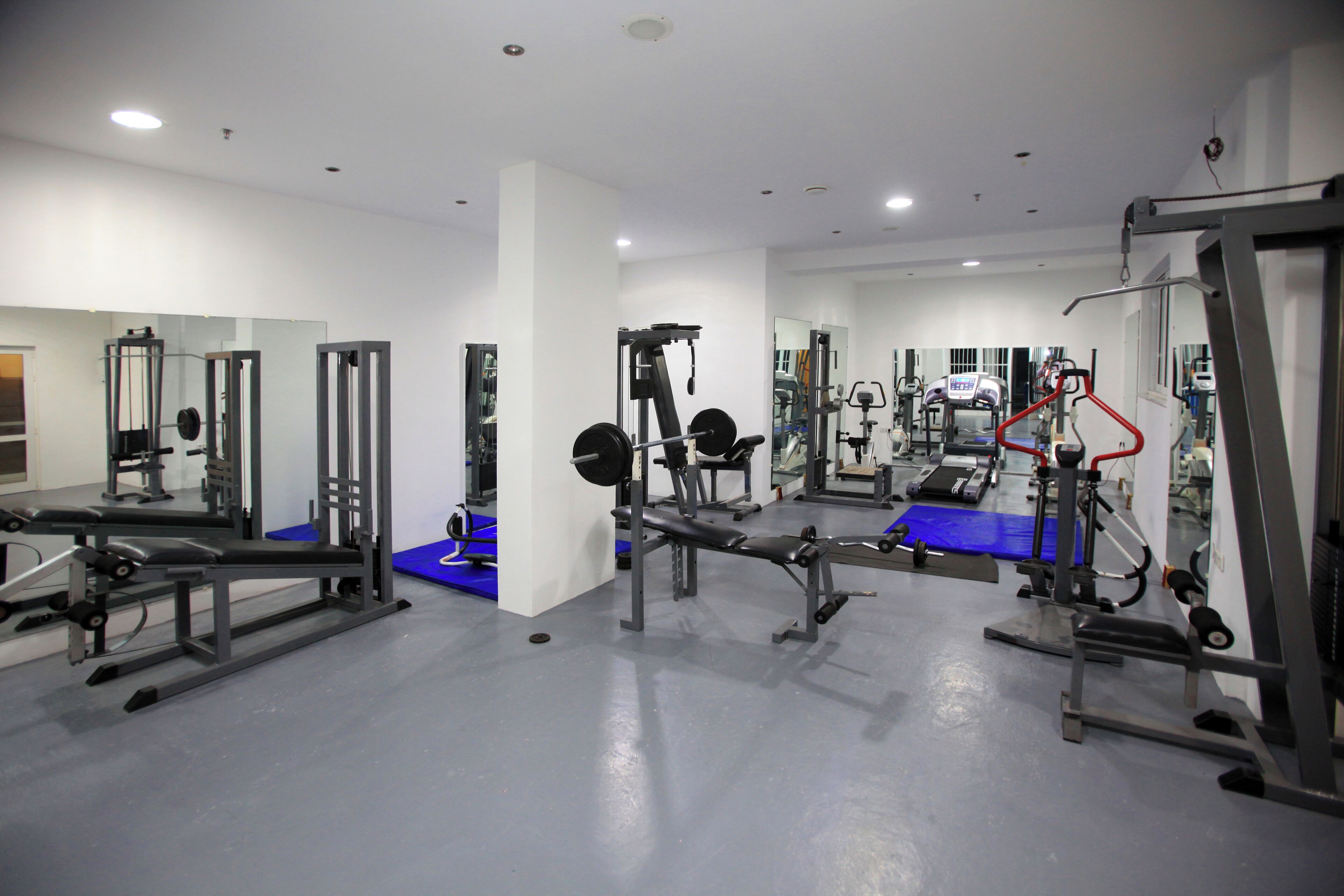 A gym with various exercise equipment, mirrors, and a blue mat on the floor.
