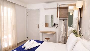 A hotel room with a bed, a vanity with a mirror, a towel rack, and a window with curtains.