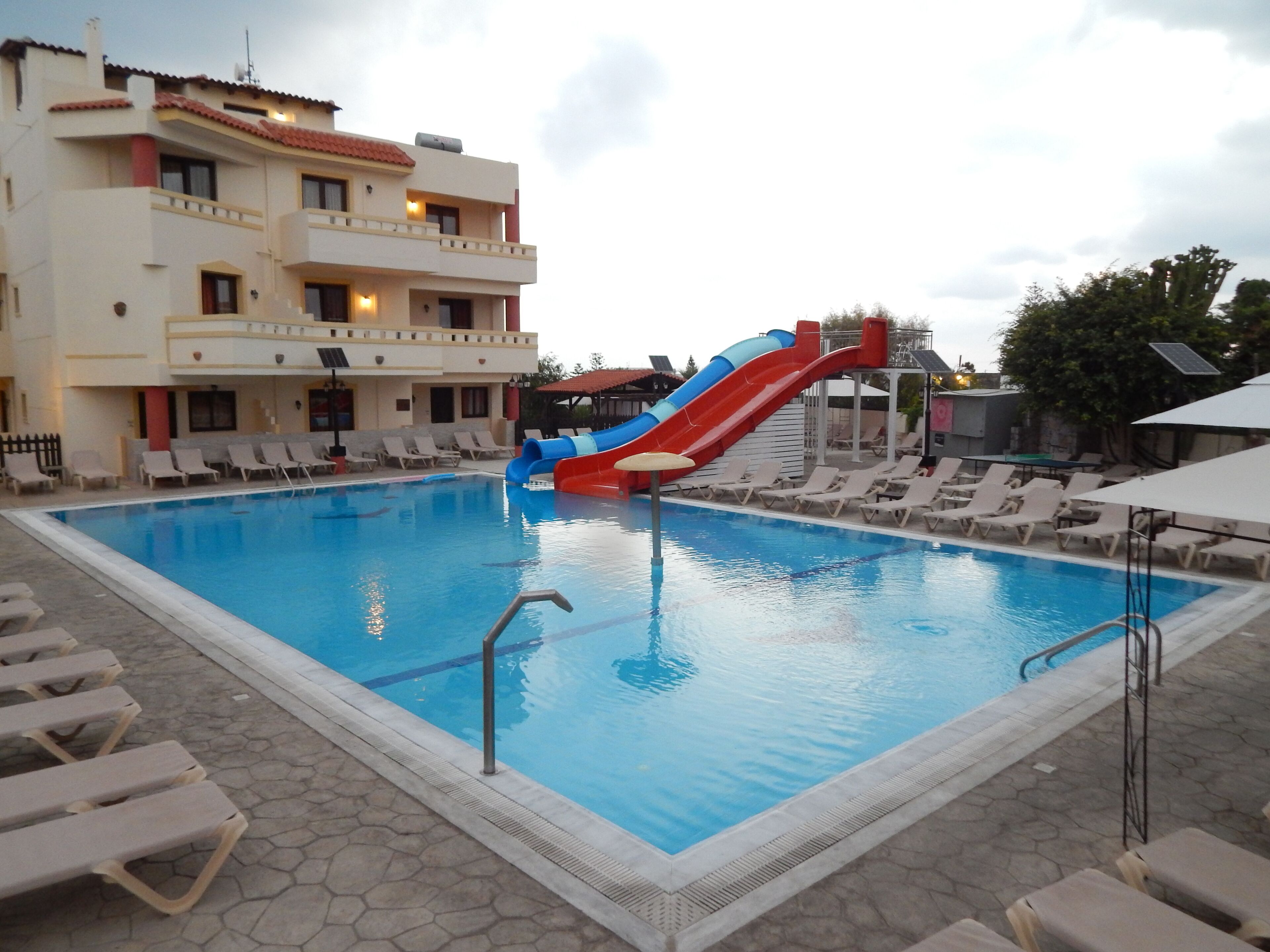 A swimming pool with a water slide, lounge chairs, and a building with balconies.