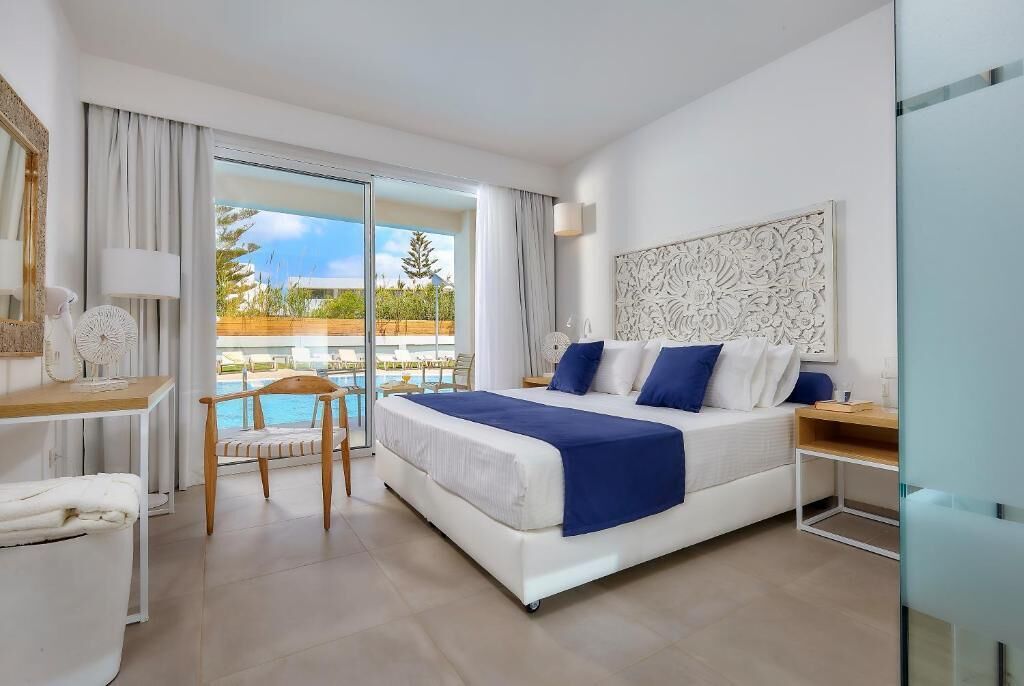 A modern bedroom with a large bed, a desk, a chair, and a view of a pool.