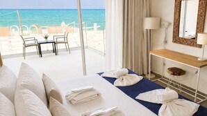 A hotel room with a bed, a desk, a chair, a table, and a view of the beach. - St. Constantin Beach Hotel and Spa (Hersonissos)